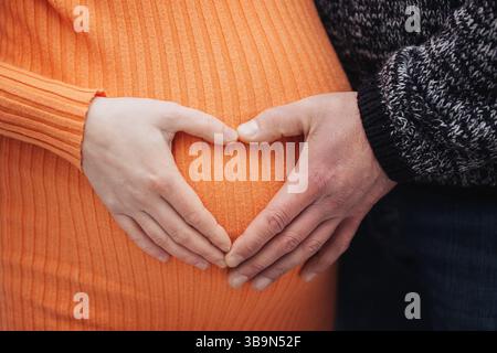 Couple enceinte mains coeur. Homme et femme sur le ventre. Maternité amour et soins. Famille attendant bébé. Heureux moment de grossesse. Banque D'Images