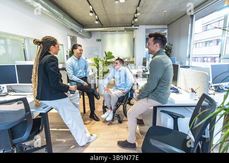 Collègues ayant une conversation dans un bureau moderne, montrant l'inclusion et le travail d'équipe avec un collègue handicapé participant activement à la discussion Banque D'Images