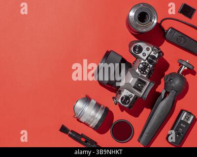 Lieu de travail de photographe avec appareil photo reflex numérique, objectif, tablette à stylet et accessoires sur fond rouge. Concept appareil photo, photographie, contenu visuel. Plat Banque D'Images