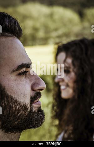 Gros plan vertical d'une vue de profil d'un visage d'homme barbu souriant au premier plan et d'un visage de femme souriant de profil en arrière-plan, naturel Banque D'Images