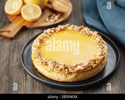 Tarte au citron végétalienne ou gâteau au citron, noix hachées décorées de façon moderne. Délicieuse tarte au citron entière sur plaque sur fond en bois. Esthétique du traditionnel Banque D'Images