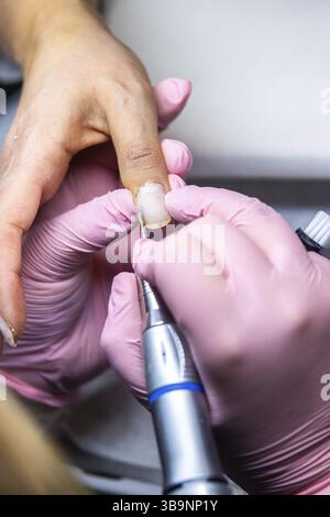 Gros plan des mains d'une manucure experte à l'aide d'une lime électrique pour le soin des ongles sur le doigt d'un client Banque D'Images