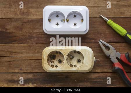 Deux prises - une ancienne grillée avec des contacts fondus et une nouvelle. EQUIPEMENT électrique, tournevis et pinces sur fond de bois ancien. Remplacement Banque D'Images