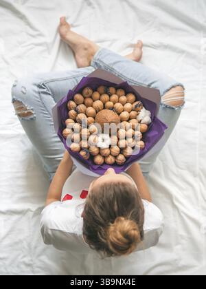 Jeune femme assise sur le lit avec noix de coco et de bouquet dans l'alimentation des mains. Vue de dessus sur les jeunes femme hipster en jean déchiré au genou avec une rare Banque D'Images