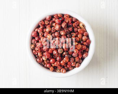 Empiler avec des baies de poivre rose séchées sur une table en bois blanc. Vue rapprochée du poivre rose. Vue de dessus ou à plat Banque D'Images