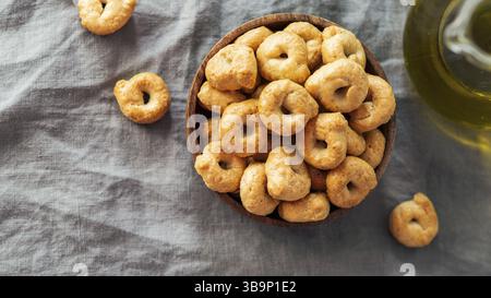 Taralli ou tarallini de snack italien traditionnel dans un bol en bois sur fond de serviette en lin gris. Plan rustique de taralli apéritif avec espace de copie. Haut Banque D'Images