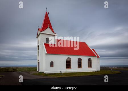 Église Ingjaldsholskirkja à Ingjaldsholl sur la péninsule de Snaefellsnes, Islande, avec des murs en béton blanc et un toit rouge, ciel nuageux. Banque D'Images