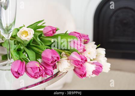 Bouquet vibrant ou tulipes roses et blanches fraîches est élégamment disposé sur une table en verre dans un fond de salon blanc. Décoration. Ambiance festive, h Banque D'Images