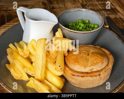 Cuisine de pub britannique traditionnelle composée de croustilles de tarte, petits pois et sauce en gros plan Banque D'Images