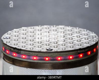 Gros plan d'une surface circulaire métallique avec un motif texturé, avec une rangée de lumières LED rouges autour du bord. Le fond est flou, empha Banque D'Images