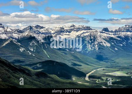 Vue panoramique sur les sommets spectaculaires des Rocheuses canadiennes avec des vallées verdoyantes et des routes sinueuses sous un ciel partiellement nuageux en été. Banque D'Images