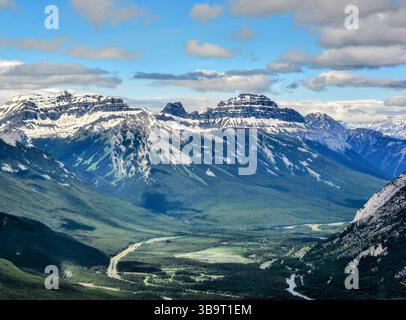 Vue panoramique sur les sommets spectaculaires des Rocheuses canadiennes avec des vallées verdoyantes et des routes sinueuses sous un ciel partiellement nuageux en été. Banque D'Images