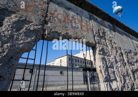 Segment fissuré du mur de Berlin avec barre d'armature exposée et la montgolfière Welt dans le ciel, capturé dans le centre-ville de Berlin. Banque D'Images