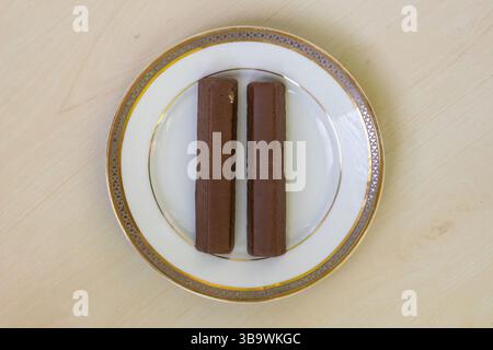 Deux biscuits à l'eau enrobés de chocolat avec de la crème au chocolat sont assis sur une assiette en céramique blanche au sommet d'une table en bois. Un en-cas délicieux parfait pour satisfaire y Banque D'Images