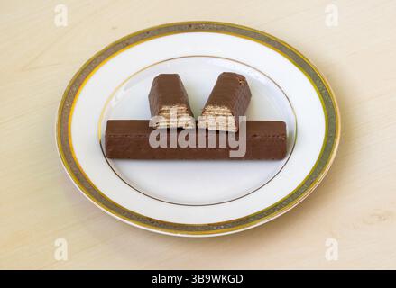 Délicieux biscuits à l'eau enrobés de chocolat, croustillants, avec de la crème au chocolat sur une plaque en céramique blanche, reposant sur une table en bois. Banque D'Images