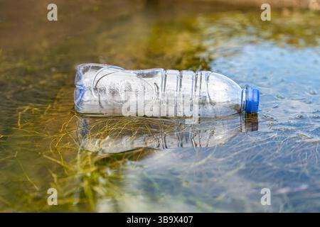 Bouteille en plastique jetée dans une rivière et polluant l'environnement par les humains. Banque D'Images