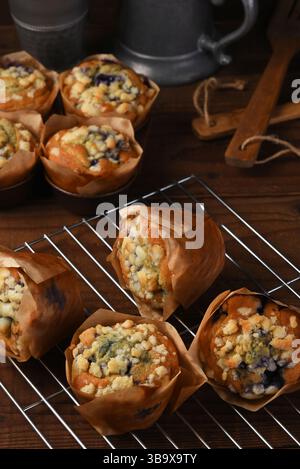 Muffins aux myrtilles fraîches cuits sur une grille de refroidissement dans une cuisine en bois rustique avec des ustensiles en bois et une théière en métal. Banque D'Images