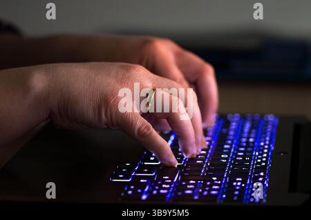 Gros plan des mains d'une femme avec le rétroéclairage d'un clavier d'ordinateur portable, clavier rétroéclairé Banque D'Images