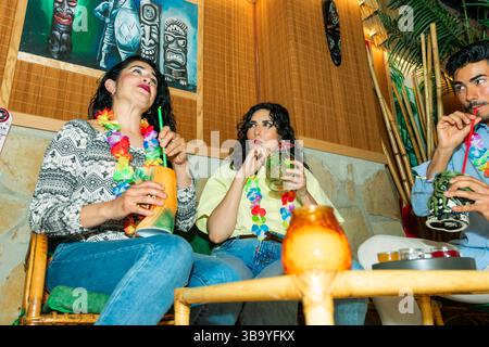 Trois amis se détendent et dégustent des cocktails tropicaux colorés dans un bar tiki Banque D'Images