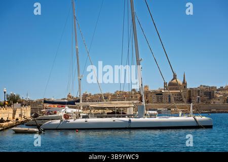 Catamaran à voile blanc ancré dans la mer calme près du front de mer avec vue sur la ville historique sous un ciel bleu clair. Thèmes du transport maritime, des voyages Banque D'Images