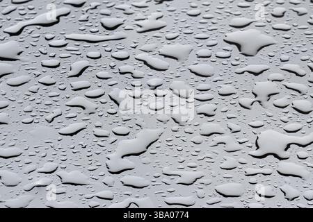 De délicates gouttes de pluie s'accrochent à une surface en verre, formant des motifs complexes qui scintillent dans la lumière discrète d'une journée grise et nuageuse. Le fond fe Banque D'Images