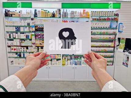 Mains de pharmacien tenant un papier avec une silhouette de tête avec un coeur à l'intérieur, symbolisant la santé mentale et le bien-être, sur les étagères de la pharmacie backdr Banque D'Images