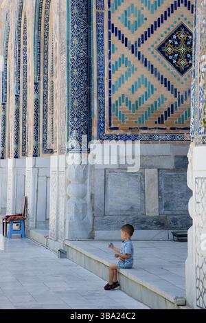 Un petit garçon jouait à Ulugh Bek Madrassah sur la place Registan, Samarcande, Ouzbékistan Banque D'Images