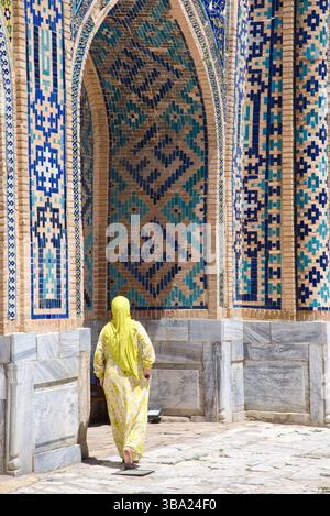 Femme en foulard et robe jaune traditionnelle entre dans l'arche à Tilya-Kori Madrasa sur la place Registan Samarcande Ouzbékistan Banque D'Images