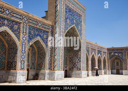 Une façade ornée de mosaïque et décorée et des arches avec femme avec un parapluie dans la madrasa Tilya-Kori sur la place Registan Samarcande en Ouzbékistan Banque D'Images
