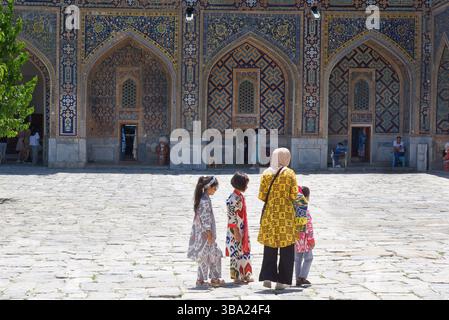 Femme en foulard avec trois enfants en tenue traditionnelle dans la Madrasa Tilya-Kori dans Registan Square Samarkand en Ouzbékistan Banque D'Images