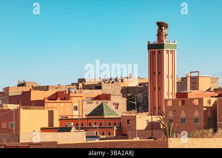 Architecture marocaine traditionnelle avec un minaret éminent s'élevant au-dessus des toits d'une ville, baigné par la lumière chaude du soleil d'un ciel bleu clair Banque D'Images