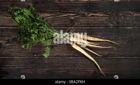 Bouquet de racines de panais avec des feuilles vertes sur une planche de bois foncé rustique, vue d'en haut, Liptovsky Hradok, Slovaquie, Europe Banque D'Images