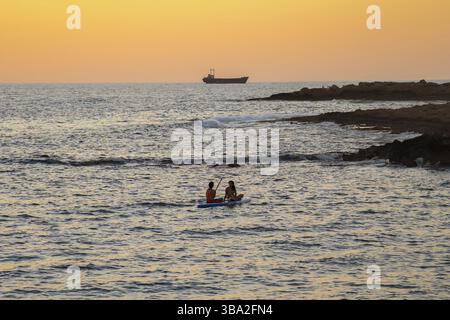 Deux filles s'assoient à bord dans la mer méditerranée tranquille au coucher du soleil dans la ville de paphos à chypre. Silhouettes de 2 filles pagayant sur paddle board à Banque D'Images