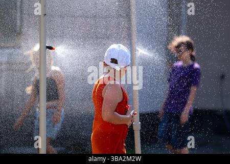 Les enfants jouent sous des gicleurs dans la chaleur intense de l'été, courant à travers les nuages d'eau brumeuse. Le spray rafraîchissant offre soulagement, rire et bouger Thr Banque D'Images