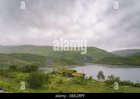 Maison d'été en bois norvégienne (Hytte) donnant sur le lac pittoresque, Norvège, Scandinavie. Chalet au bord du lac en milieu rural. Cabane au toit de tourbe sur le lac. R L'herbe typique Banque D'Images
