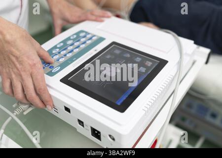 Le médecin cardiologue effectue une procédure d'électrocardiographie sur un homme allongé sur un lit à l'hôpital.Test ECG d'un homme dans une clinique moderne.Diagnostic, voiture saine Banque D'Images