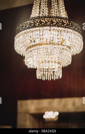 Grand lustre en cristal avec de nombreuses petites lumières scintillantes suspendues à l'intérieur de la chambre rouge, photo portrait vertical Banque D'Images