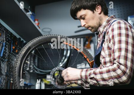 Jeune réparateur caucasien répare la roue de VTT dans un atelier de vélo. Fixation du vélo. Prendre soin de vous les roues. Homme mécanicien travaillant dans le garage. Banque D'Images