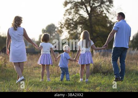 Famille heureuse : mère, père, enfants, fils et filles dans la nature au coucher du soleil. Parents et enfants marchent ensemble. La grande famille Banque D'Images