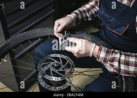 Homme mécanicien travaillant dans un atelier de réparation de vélos, mécanicien réparant le vélo à l'aide d'un outil spécial, portant des gants de protection. Jeune fixin de technicien de maintenance attrayant Banque D'Images