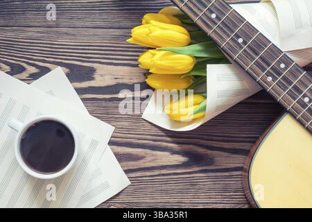 Belle musique de fond au printemps. Guitare, tulipes jaunes, tasse de café, pas encore de page sur un fond de bois sombre. Profondeur de champ. Ph coloriage Banque D'Images
