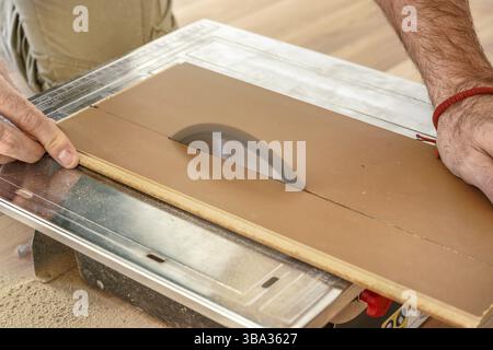 Homme coupant des planches de plancher stratifiées sur scie circulaire, détail sur les mains tenant le panneau en bois et l'anneau rotatif, photo d'illustration d'amélioration de l'habitat, Liptov Banque D'Images