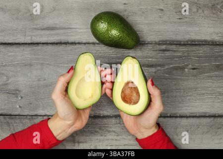 Main de femme tenant deux moitiés d'avocat, graine visible, poire d'avocat entière à côté, Liptovsky Hradok, Slovaquie, Europe Banque D'Images