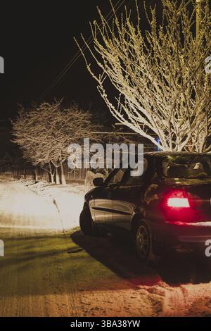 Les phares d'une voiture noire éclairent la route enneigée en hiver Banque D'Images
