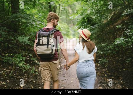 Couple tenant les mains marchant dans la forêt, vue arrière. Aventure, voyage, tourisme, randonnée, gens. Vue arrière de deux personnes transportant un sac à dos en marchant t Banque D'Images