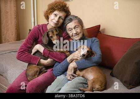 La femme aînée et sa fille adulte avec deux chiens dachshund sur un canapé à l'intérieur passent du temps heureux, portrait. Thème de la relatio mère et fille Banque D'Images