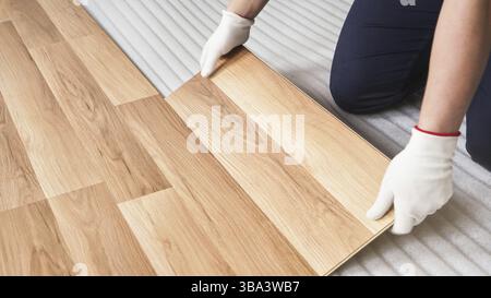 Installation de plancher stratifié, détail sur les mains des travailleurs dans des gants blancs ajustant des carreaux de bois, sur la couche de base en mousse blanche, Liptovsky Mikulas, Slovaquie, Europ Banque D'Images
