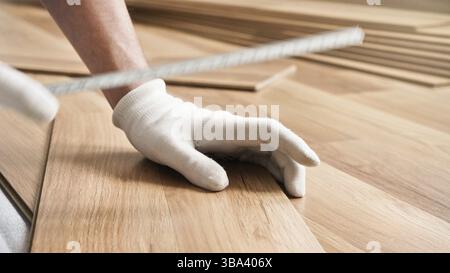 Installation de plancher stratifié, détail sur les mains de l'homme dans des gants blancs, tenant le ruban à mesurer sur des carreaux de bois, Liptovsky Mikulas, Slovaquie, Europe Banque D'Images