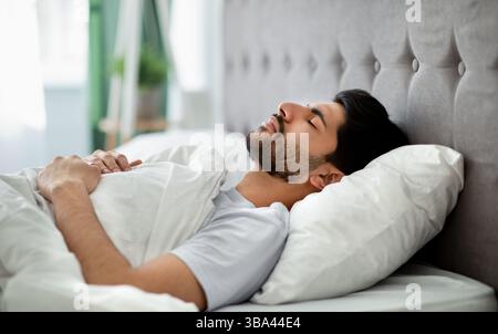 Sommeil profond chez les hommes. Un jeune homme arabe dormant paisiblement dans son lit confortable à la maison, allongé avec les yeux fermés sur le dos Banque D'Images