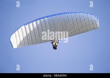 Ein Gleitschirm fliegt in den Himmel unter einem mehrfarbigen Gleitschirm. Mann unter Fallschirm Banque D'Images